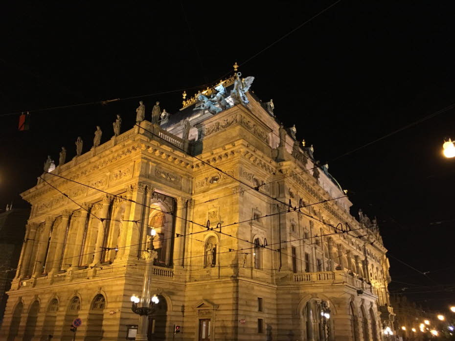 Oper bei Nacht: Staatsoper in Prag: Das schöne klassizistische Gebäude der Staatsoper kann nicht unbemerkt bleiben. Der Stil ist erkennbar an dem Fries, der den dreieckigen Giebel über der Loggia mit charakteristischen Säulen schmückt. Dionysos, ein Förde\