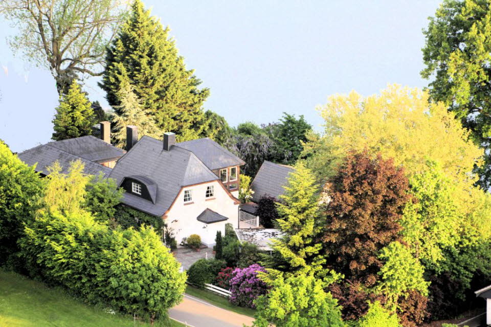 Die Gebäude Belauer Straße 37 sind der Startpunkt der Fahrt. Die Gebäude lassen sich stilistisch als moderne Interpretation eines klassischen Landhauses einordnen: Landhausstil: Dachform, Volumen, Gartenintegration. Moderne Elemente: klare Fassaden, reduz