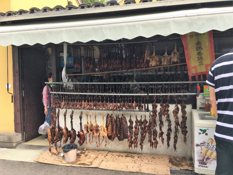 Gegrilltes Geflügel und Vögel auf dem  Markt von Xinchang:Lebendes Geflügel in Käfigen ist auf chinesischen Märkten ein üblicher Anblick. Die Tiere werden in der Regel von den Verkäufern vor Ort oder auch von den Kunden daheim geschlachtet. Als Folge aus 